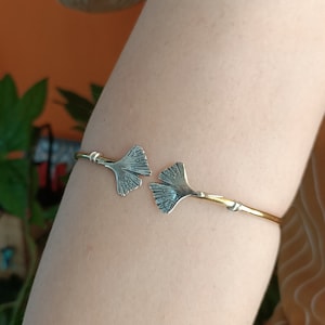 Puede incluir: Un brazalete de brazo dorado con dos diseños de hojas de ginkgo. El brazalete es abierto y ajustable.