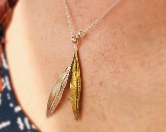 Könnte beinhalten: Eine silberne Kettenkette mit einem Anhänger aus zwei Blättern, einem goldenen und einem silbernen.
