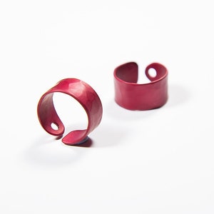 Puede incluir: Dos anillos de metal rojo, uno con acabado martillado y el otro con superficie lisa.