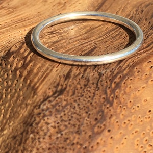 Op de afbeelding: Een eenvoudige zilveren bandring met een glad, afgerond oppervlak. De ring wordt getoond op een houten oppervlak. Ronde draadring.