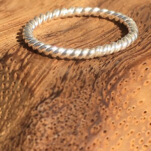 Op de afbeelding: Een zilveren ring met een dubbele gevlochten draad. De ring ligt op een houten oppervlak.