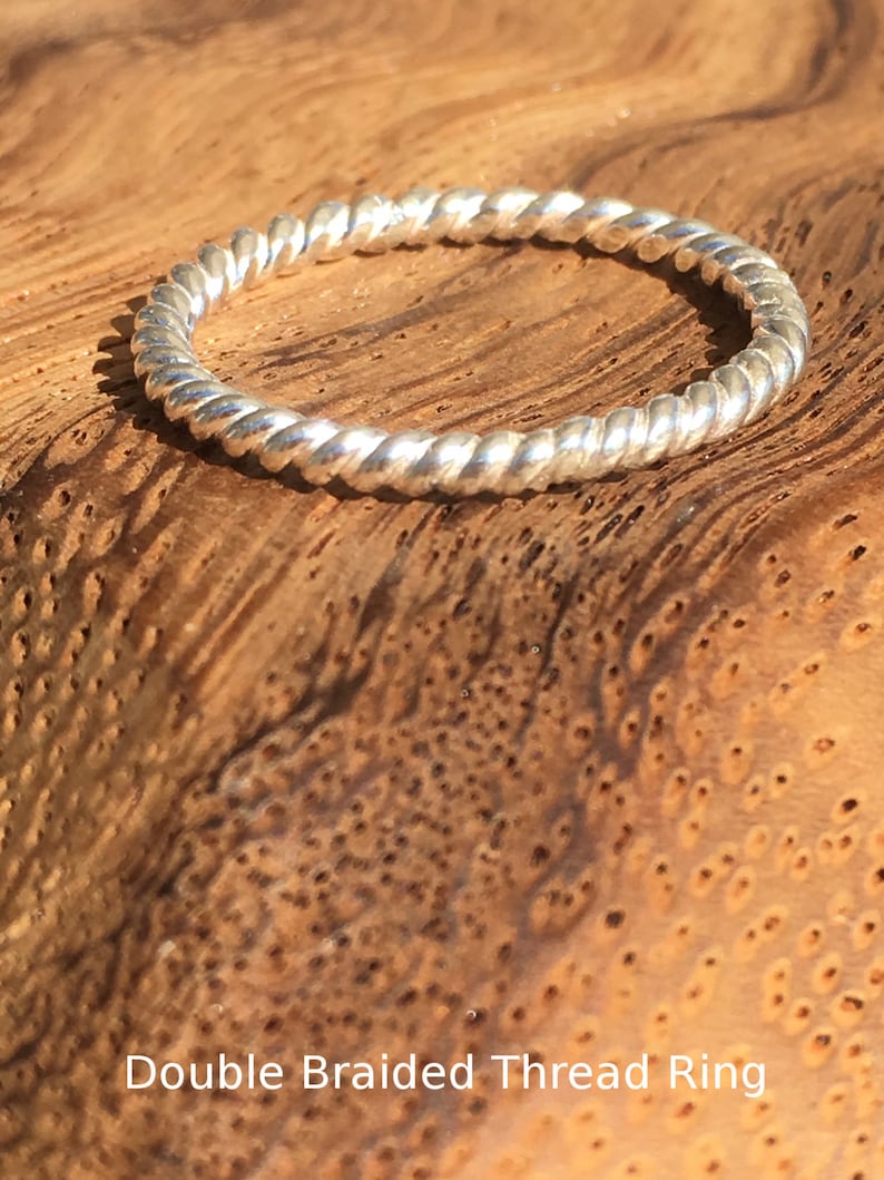Op de afbeelding: Een zilveren ring met een dubbele gevlochten draad. De ring ligt op een houten oppervlak.
