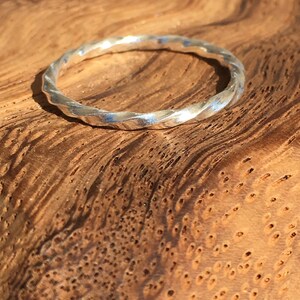 Op de afbeelding: Een zilveren ring met gedraaide vierkante draad op een houten oppervlak.