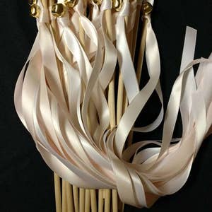 May include: A bunch of ivory satin ribbon wands with gold bells attached to the ends. The wands are tied together and the ribbons are flowing.