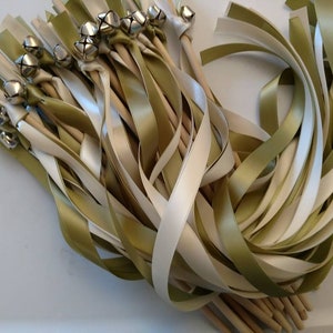 May include: A bunch of ivory and olive green satin ribbon wands with silver bells attached to the ends. The wands are tied together with a wooden stick.