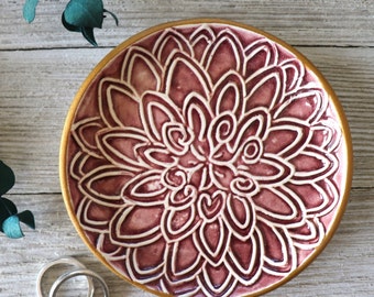 Könnte beinhalten: Eine Keramik-Ring Schale mit goldfarbenem Rand und einem erhabenen Blumendesign in Burgunder- und Weißtönen.