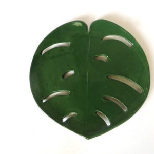 May include: A green ceramic dish shaped like a monstera leaf. The dish has cutouts in the shape of the leaf's holes.