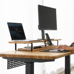 May include: A black and wood standing desk with a black monitor stand, a laptop stand, and a black keyboard and mouse. The desk has a black metal frame and a wood top.