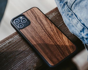 May include: A wooden phone case with a dark brown wood grain pattern and a black border. The case has a cutout for the phone's camera lenses.