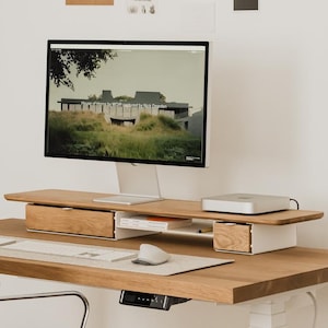 May include: A modern home office setup featuring a wooden desk with a computer monitor, keyboard, and mouse. A black office chair and a small desk lamp are also present. The desk is 150 cm wide and has a height-adjustable base.