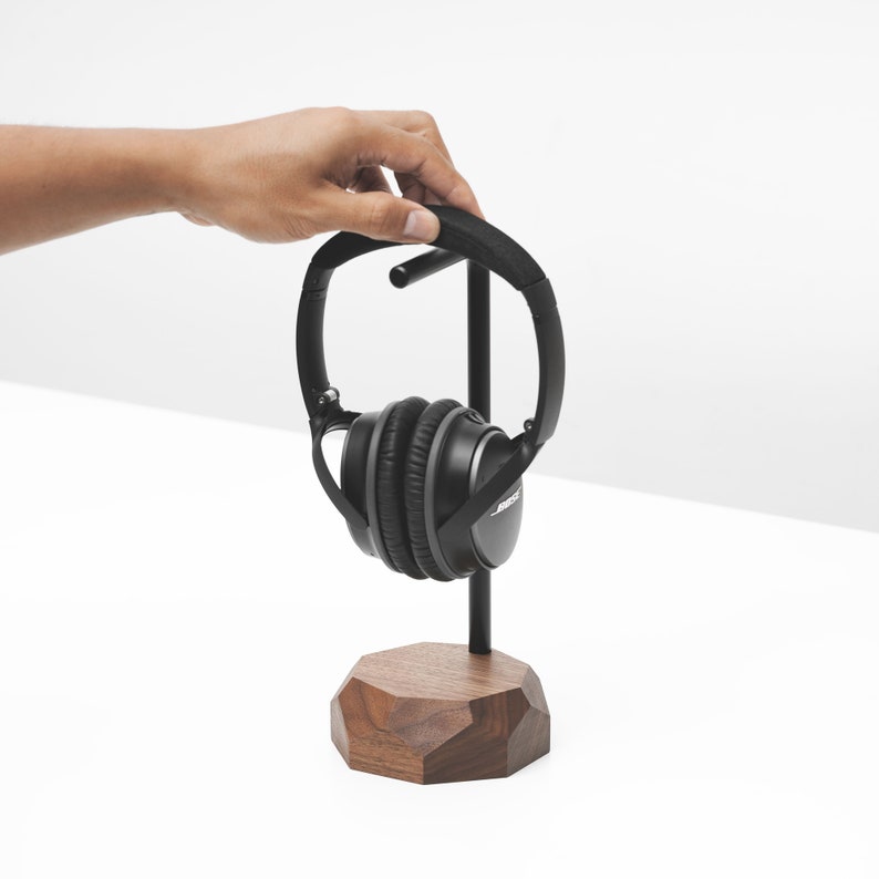 May include: A black headphone stand with a wooden base. The stand has a metal rod and a black headphone is hanging on it.