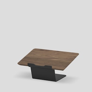 May include: A laptop stand featuring a dark brown wood grain platform supported by a matte black metal base. The platform is angled upward, and the black metal base includes a small front lip to secure a device in place on the flat surface.