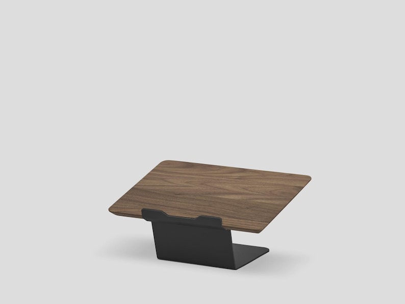 May include: A laptop stand featuring a dark brown wood grain platform supported by a matte black metal base. The platform is angled upward, and the black metal base includes a small front lip to secure a device in place on the flat surface.