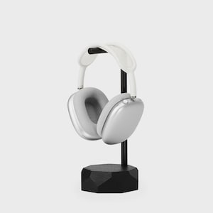 May include: Silver headphones with a white headband, resting on a black stand with a geometric base.