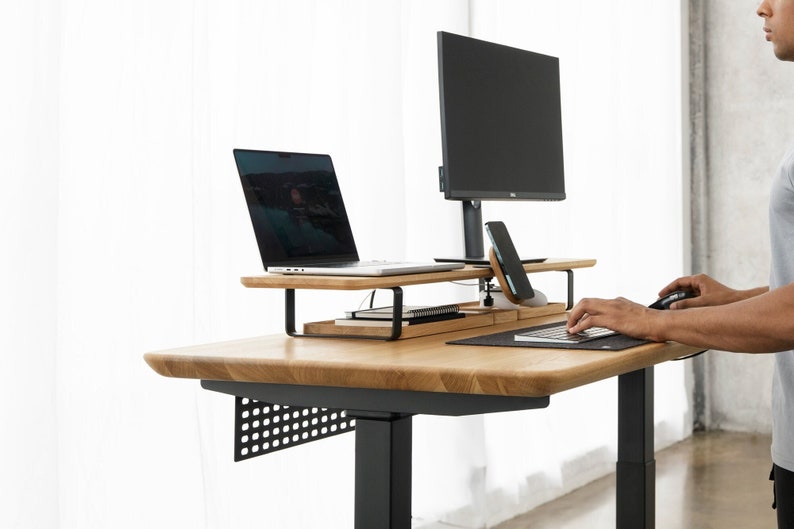 May include: A black and wood standing desk with a black monitor stand, a laptop stand, and a black keyboard and mouse. The desk has a black metal frame and a wood top.