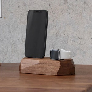 May include: A wooden charging stand with a geometric design, holding a black smartphone and a white smartwatch.