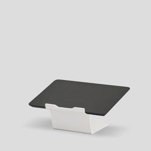 May include: A black rectangular tablet stand featuring a smooth, flat surface angled for viewing, supported by a sturdy white metal base with a front lip to secure the device in place. The design is clean and functional, providing a stable platform.