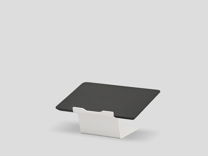 May include: A black rectangular tablet stand featuring a smooth, flat surface angled for viewing, supported by a sturdy white metal base with a front lip to secure the device in place. The design is clean and functional, providing a stable platform.