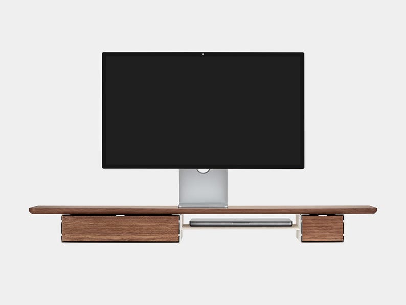 May include: A modern computer monitor sits on a wooden desk with two drawers and a shelf for a laptop. The monitor has a black screen and a silver stand. The desk is made of dark wood.