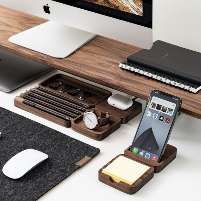 K&ouml;nnte beinhalten: Ein h&ouml;lzerner Schreibtisch-Organizer mit mehreren F&auml;chern f&uuml;r Stifte, Bleistifte, eine Uhr, ein Telefon und Haftnotizen. Der Organizer ist aus dunklem Holz gefertigt und hat ein modernes Design.