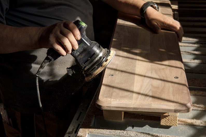 May include: A person sanding a piece of wood with a black and green electric sander.