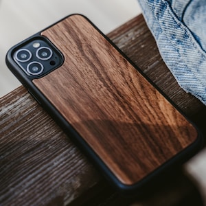 May include: A brown wood phone case with a black trim. The case has a camera lens cutout with three black circles.
