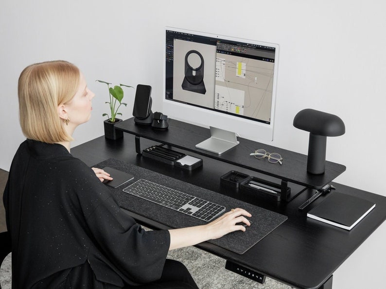 May include: A black desk with a black monitor stand, a black keyboard, a black mouse, a black lamp, and a black notebook. The desk is also equipped with a black phone charger and a black watch charger.