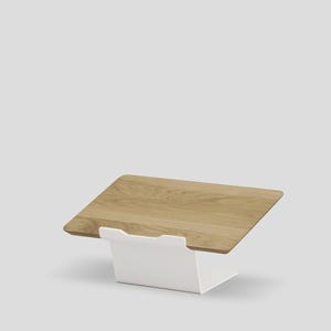 May include: A laptop stand featuring a rectangular light brown wood grain platform supported by a solid white metal base. The stand is angled upward, providing a stable surface for a device, with a clean, simple design and smooth finish.