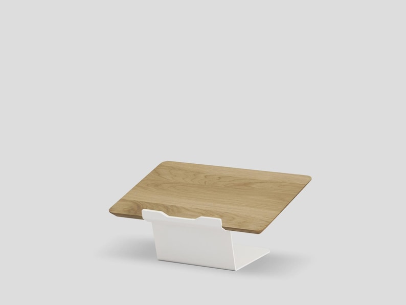 May include: A laptop stand featuring a rectangular light brown wood grain platform supported by a solid white metal base. The stand is angled upward, providing a stable surface for a device, with a clean, simple design and smooth finish.