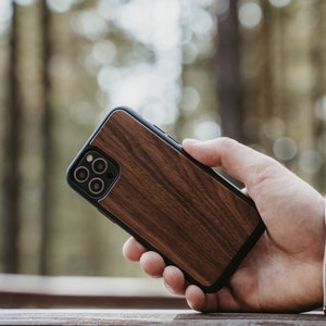 May include: A brown wood phone case with a black camera lens cutout. The case is made of real wood and has a natural grain pattern.