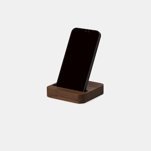 K&ouml;nnte beinhalten: Ein Holz-Telefonst&auml;nder mit dunkelbrauner Oberfl&auml;che. Ein schwarzes Smartphone ist in den St&auml;nder gestellt.