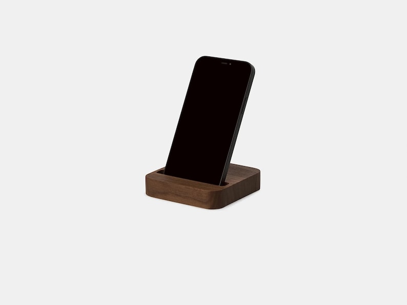 K&ouml;nnte beinhalten: Ein Holz-Telefonst&auml;nder mit dunkelbrauner Oberfl&auml;che. Ein schwarzes Smartphone ist in den St&auml;nder gestellt.