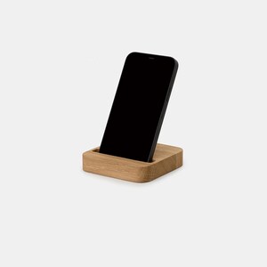 K&ouml;nnte beinhalten: Ein Holz-Telefonst&auml;nder mit einem schwarzen Smartphone, das darauf liegt. Der St&auml;nder ist aus hellem braunem Holz gefertigt und hat ein schlichtes, modernes Design.