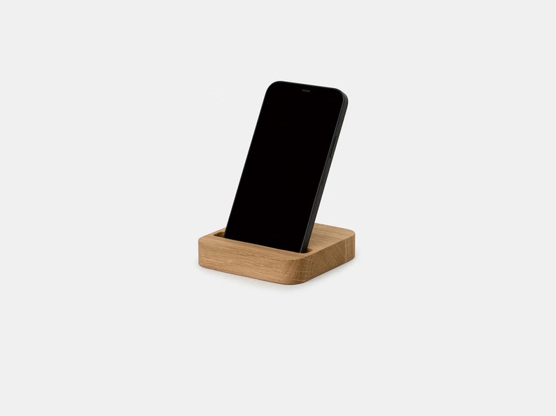 K&ouml;nnte beinhalten: Ein Holz-Telefonst&auml;nder mit einem schwarzen Smartphone, das darauf liegt. Der St&auml;nder ist aus hellem braunem Holz gefertigt und hat ein schlichtes, modernes Design.
