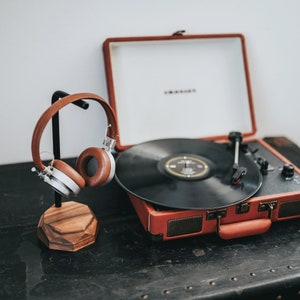 May include: A vintage-style record player with a brown wooden case and a black vinyl record on the turntable. A pair of brown headphones are on a stand next to the record player.