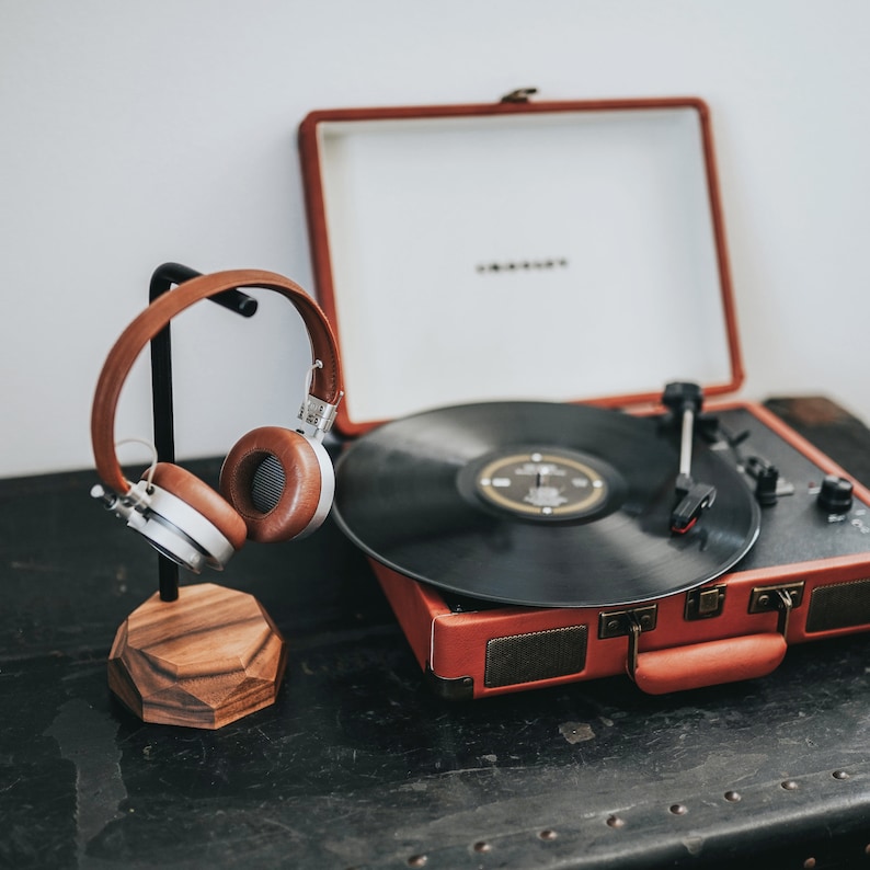 May include: A vintage-style record player with a brown wooden case and a black vinyl record on the turntable. A pair of brown headphones are on a stand next to the record player.