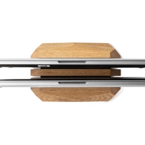 May include: Two silver laptops stacked on a wooden stand. The stand is made of light brown wood and has a hexagonal shape.