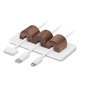 May include: A white cable tidy with three white cables and three brown wooden cable holders. The cable tidy has a rectangular base and is designed to hold various types of charging cables.