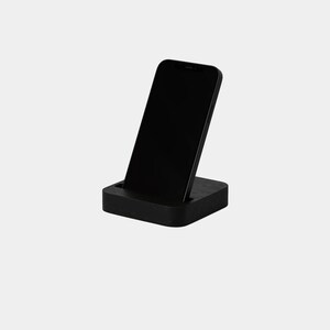 K&ouml;nnte beinhalten: Ein schwarzer Smartphone-St&auml;nder aus Holz. Der St&auml;nder ist so konzipiert, dass er ein Telefon aufrecht h&auml;lt, mit einem Schlitz, in dem das Telefon ruhen kann.