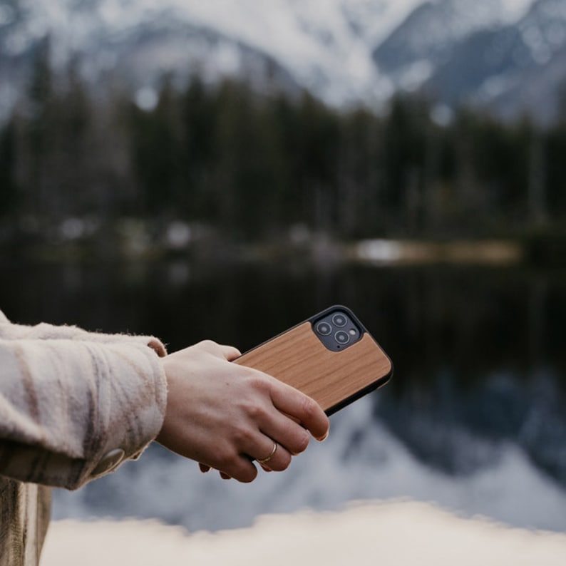 May include: A person holding a wooden phone case with a black camera lens. The case has a natural wood grain pattern.