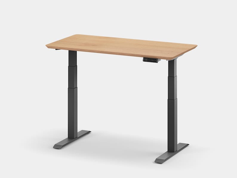 May include: A light wood-toned standing desk with a black electric lift mechanism and a rectangular tabletop. The desk has a black base with two legs.