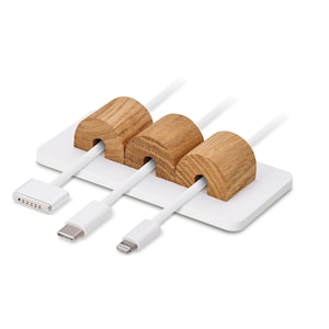 May include: A white cable tidy featuring three wooden cable holders. The cylindrical wooden holders are set on a white rectangular base. Three white cables with different connectors are inserted through the wooden holders.