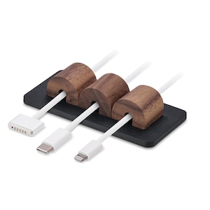 May include: A cable tidy with three slots, each holding a white cable. The tidy has a black base and three brown wooden cable holders. The cables have different connector types.