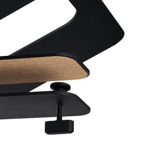 May include: A black metal desk clamp with a cork pad and adjustable screw. The clamp is designed to hold a laptop or other device. The design is modern and minimalist.