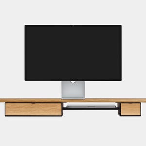 May include: A modern computer monitor with a black screen is mounted on a light wood desk. The desk has two drawers and a shelf for a laptop. The desk is made of light-colored wood with black accents.