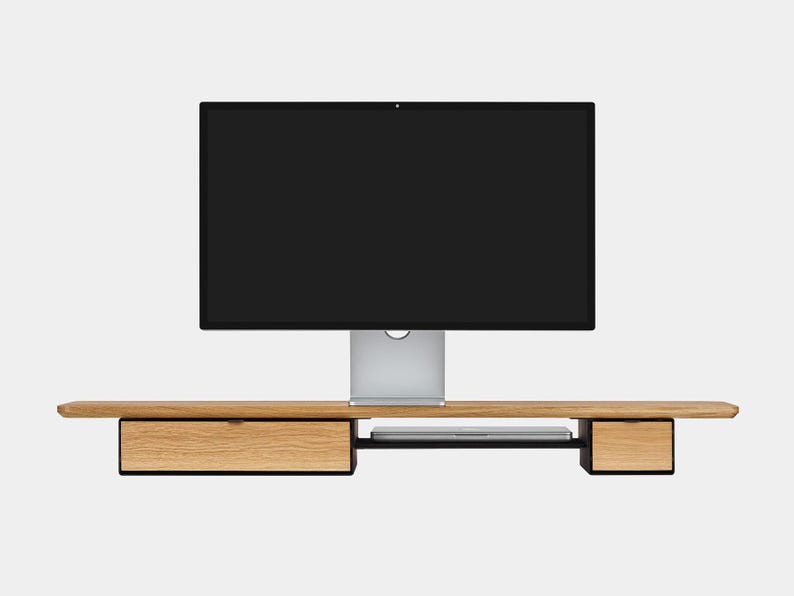May include: A modern computer monitor with a black screen is mounted on a light wood desk. The desk has two drawers and a shelf for a laptop. The desk is made of light-colored wood with black accents.