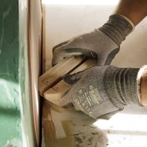 May include: A person wearing work gloves sands a piece of wood with a belt sander. The wood is light brown and has a smooth surface.