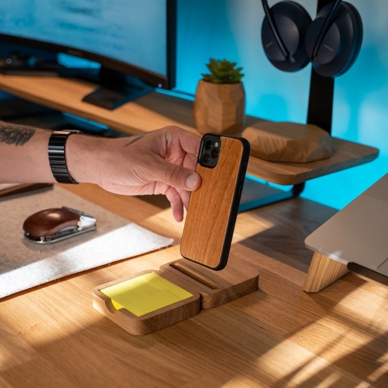 K&ouml;nnte beinhalten: Ein Holz-Telefonst&auml;nder mit einem gelben Haftnotizhalter. Der St&auml;nder ist aus hellbraunem Holz gefertigt und hat einen schwarzen Telefonhalter. Der Telefonhalter ist aus Holz und hat einen schwarzen Rand. Der St&auml;nder steht auf einem Holztisch.