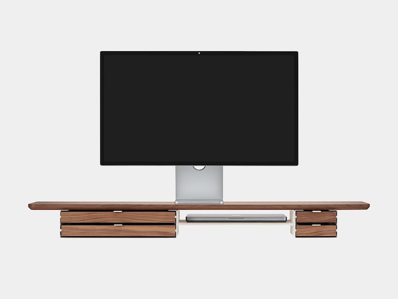 May include: A modern wooden desk with integrated drawers and a shelf for a laptop. A large computer monitor is centered above the desk. The desk is made of dark wood and has a minimalist design.