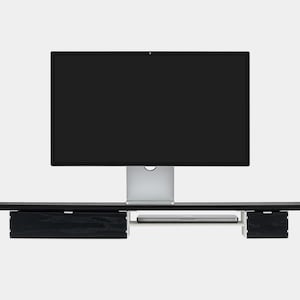 May include: A black wooden monitor stand with two drawers and a shelf for a laptop. The stand supports a large computer monitor with a silver base. The design is modern and minimalist.